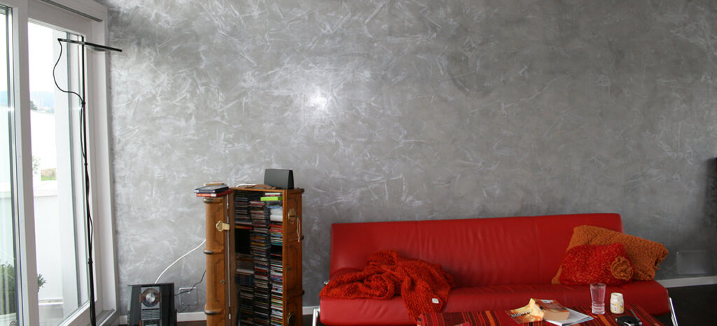 Wand mit Silberfinish, Untergrund Stucco Veniziano in Grau davor ein Rotes Sofa